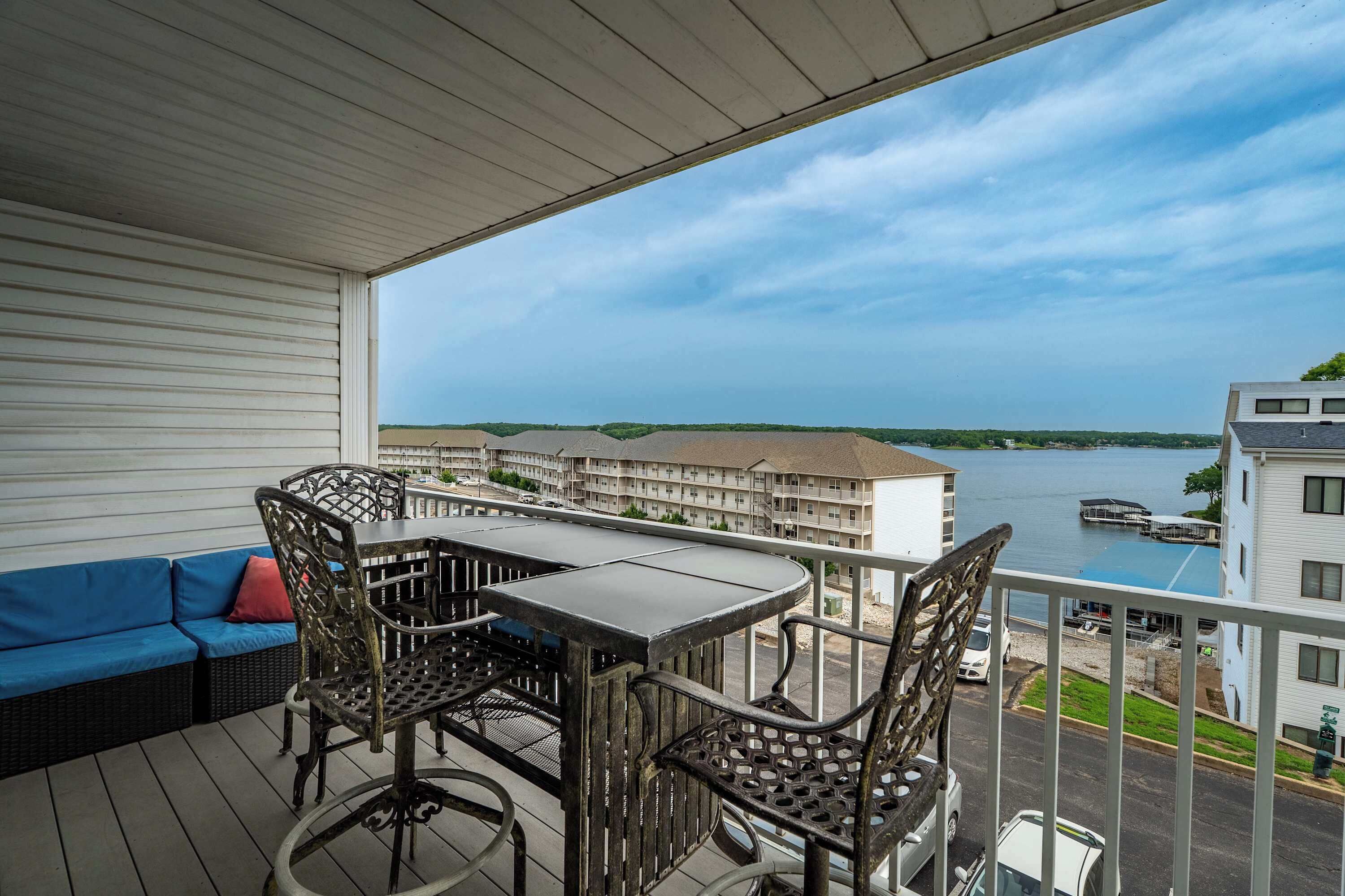 A balcony with a table and chairs, overlooking a body of water and buildings.