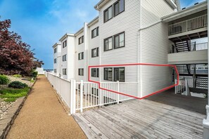 Um edifício residencial com vários andares, uma varanda de madeira e uma cerca branca.