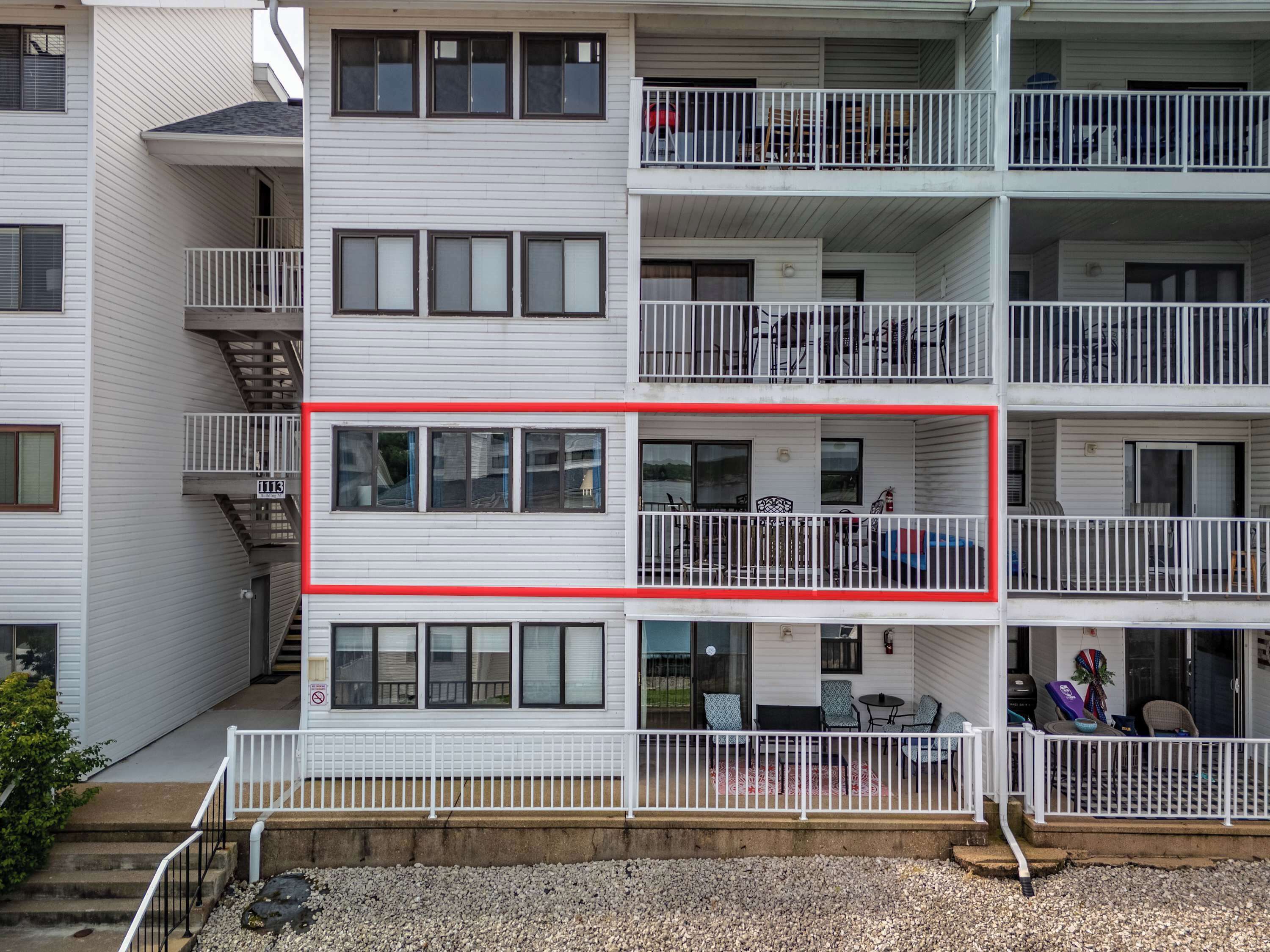 A multi-story residential building with balconies, a visible fire escape, and a gravel driveway.