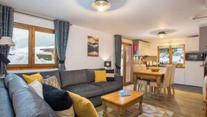 A living room with a sofa, a coffee table, and a dining area with a table and chairs. - Simply Morzine - Apartment des Montagnes (Les Gets)