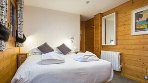 A bedroom with a bed, pillows, a nightstand, a mirror, and a radiator. - Simply Morzine - Apartment des Montagnes (Les Gets)