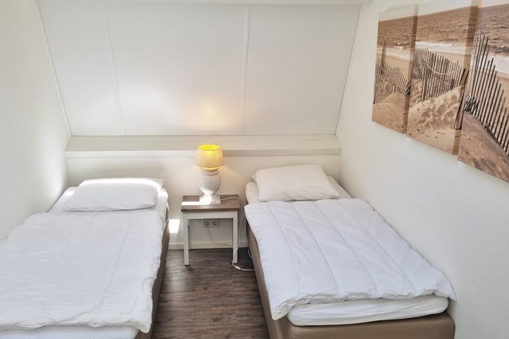 A small, single room with two beds, a nightstand with a lamp, and a wall-mounted artwork.