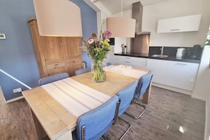 A modern kitchen with white cabinets, a wooden dining table, and blue chairs. - 4-person apartment 'ZEE' in Oostkapelle. (Oostkapelle)