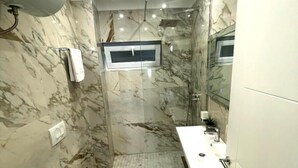 Et lille badeværelse med toilet, bidet og vask, marmorvægge og et lille vindue.