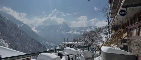 Un área de estar al aire libre cubierta de nieve con vistas a montañas, un atrapasueños y un letrero de cafetería.