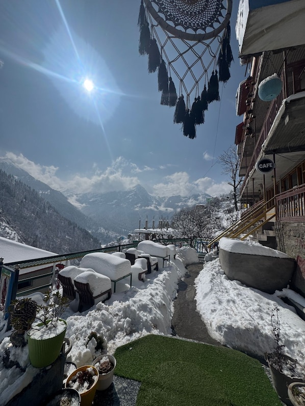 Un área de estar al aire libre cubierta de nieve con vistas a montañas, un atrapasueños y un letrero de cafetería.