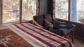 Una habitació amb un llit, dues cadires i grans finestres que donen vista a un paisatge cobert de neu.