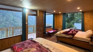 Habitació amb sostre de fusta, dos llits amb llençols estampats de flors, taula de fusta i grans finestres amb vista als arbres.