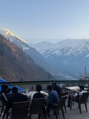 A group of people dining at an outdoor table with a mountain view. - Cafe Kush Tosh And Stay (Bhuntar)