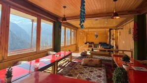 Un interior de fusta amb taula vermella, decoracions penjades i grans finestres.
