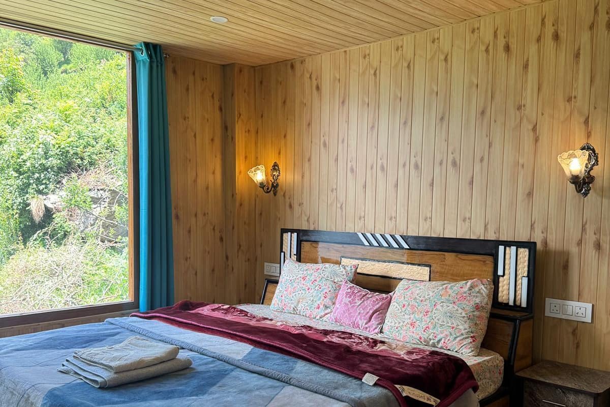 Une pièce aux murs lambrés, comprenant un lit, deux appliques murales, une fenêtre avec des rideaux et une table de chevet.