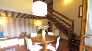 A dining area with a wooden table, white chairs, a vase with flowers, and a staircase.