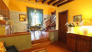 A kitchen with wooden cabinets, a dining area with a table and chairs, a staircase, and a living area with a sofa.