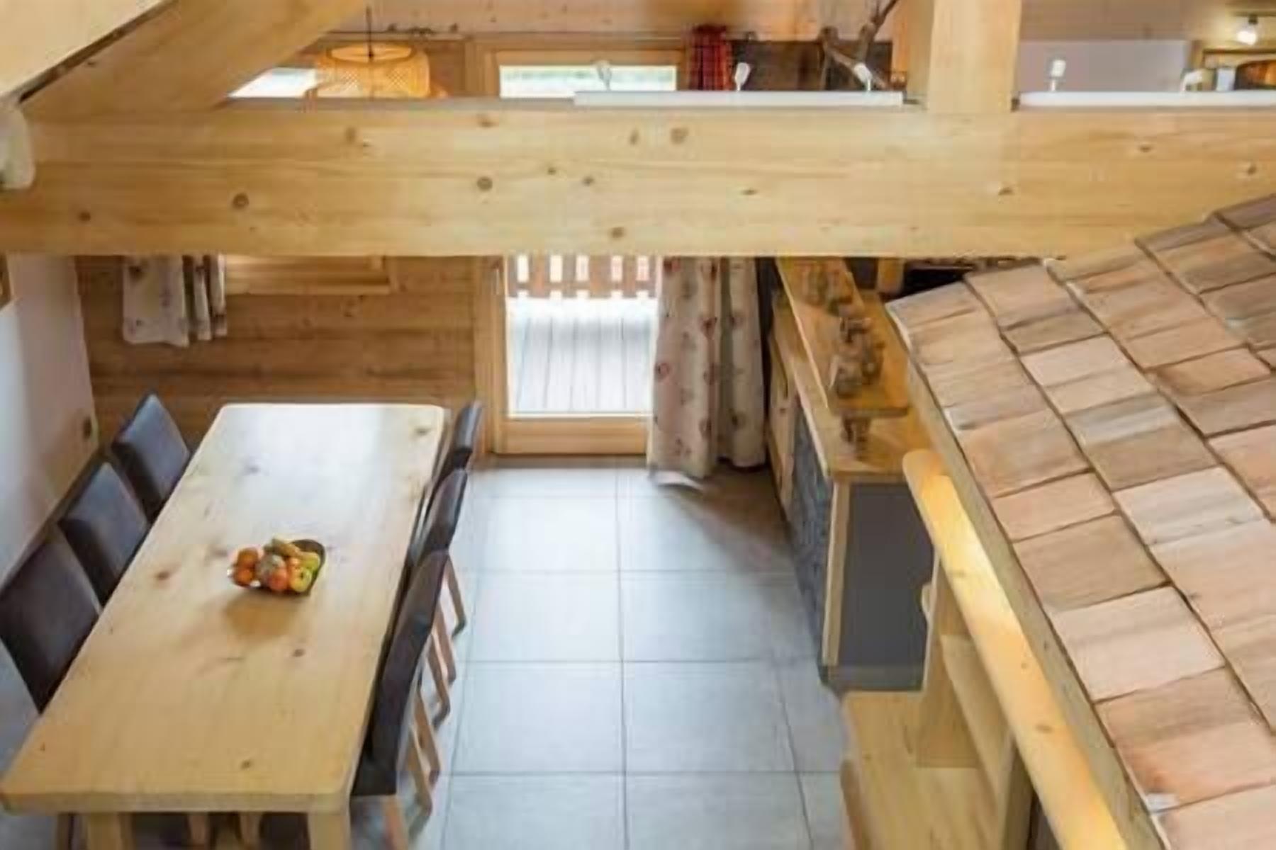 Un coin repas en bois avec une table et des chaises, un espace cuisine avec un fourneau et un sol carrelé.