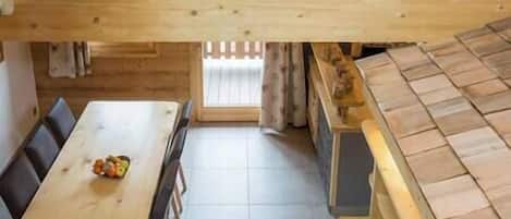 Un coin repas en bois avec une table et des chaises, un espace cuisine avec un fourneau et un sol carrelé.