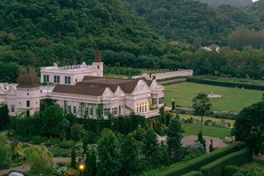 Un edificio grande, blanco e histórico con múltiples cúpulas y torres, rodeado de exuberante follaje y un jardín bien cuidado.