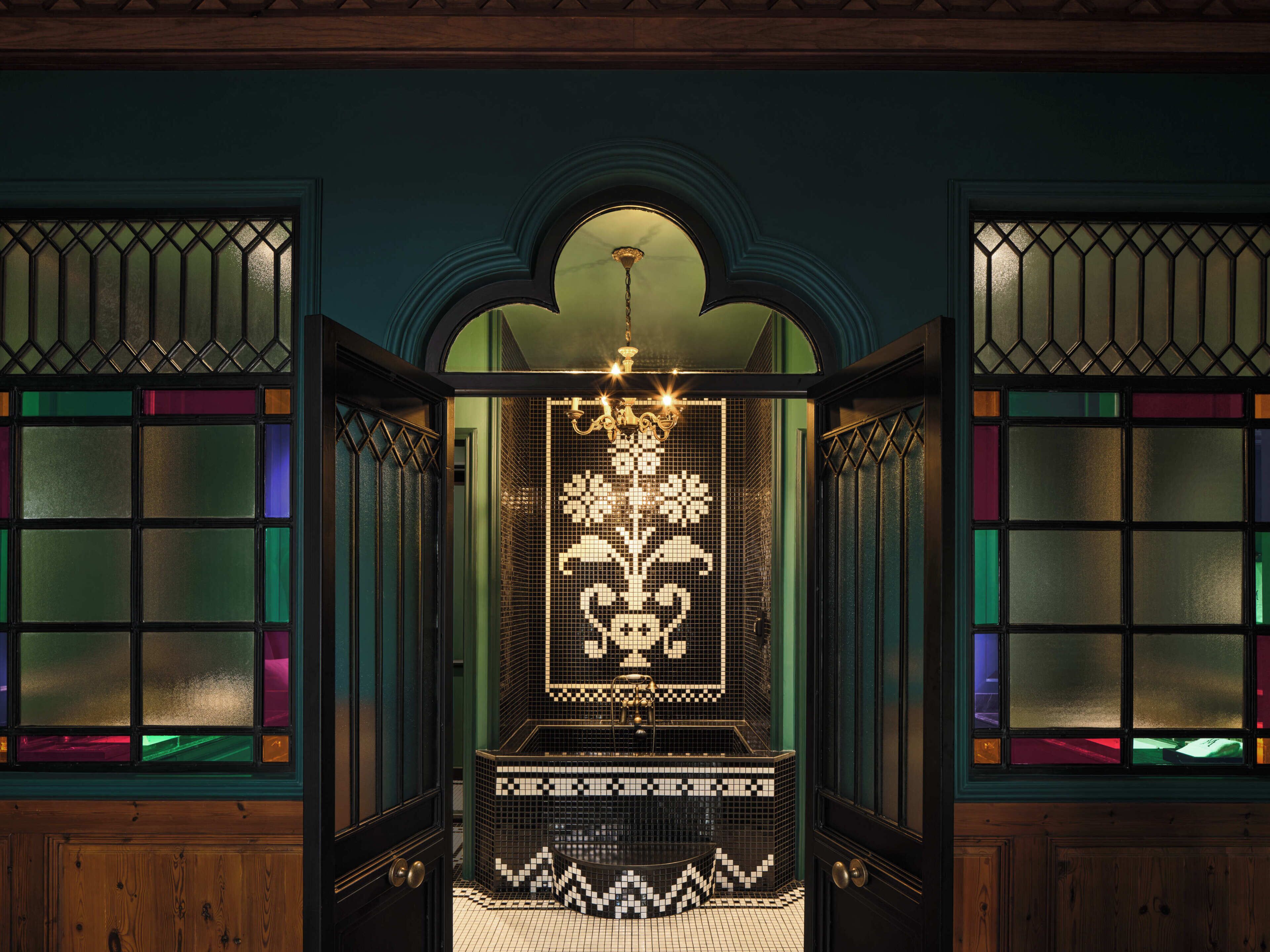 Una habitación con suelo de baldosas, un candelabro y una puerta con un panel de vidrio decorativo.