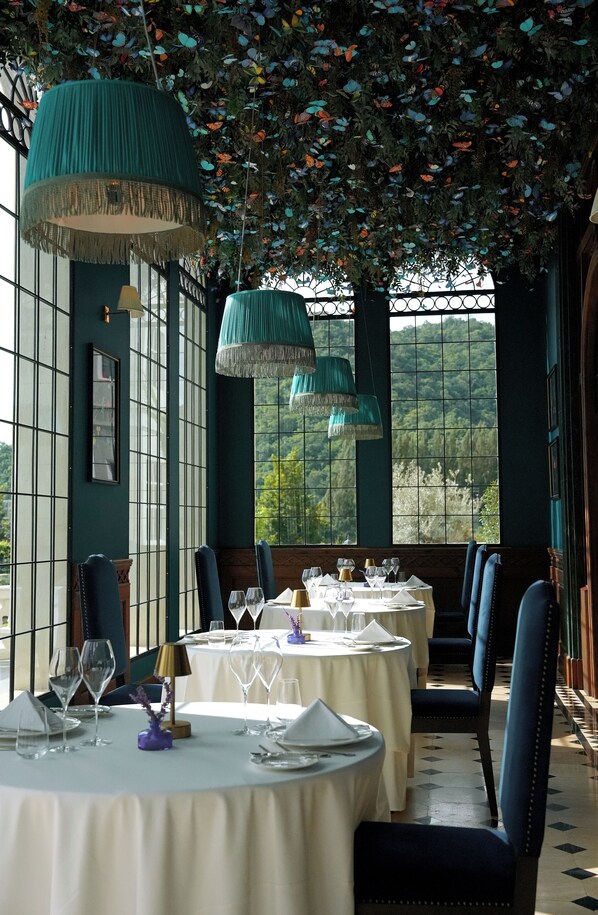 Un restaurante con mesas redondas, sillas azules y lámparas verdes colgantes.