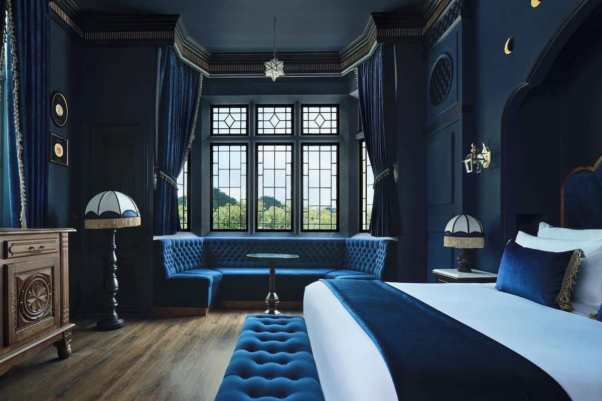 Quarto com uma cama grande, um banco e janela com vista.