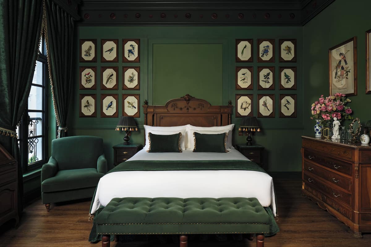 Quarto com uma cama grande, paredes verdes e ilustrações de pássaros emolduradas.