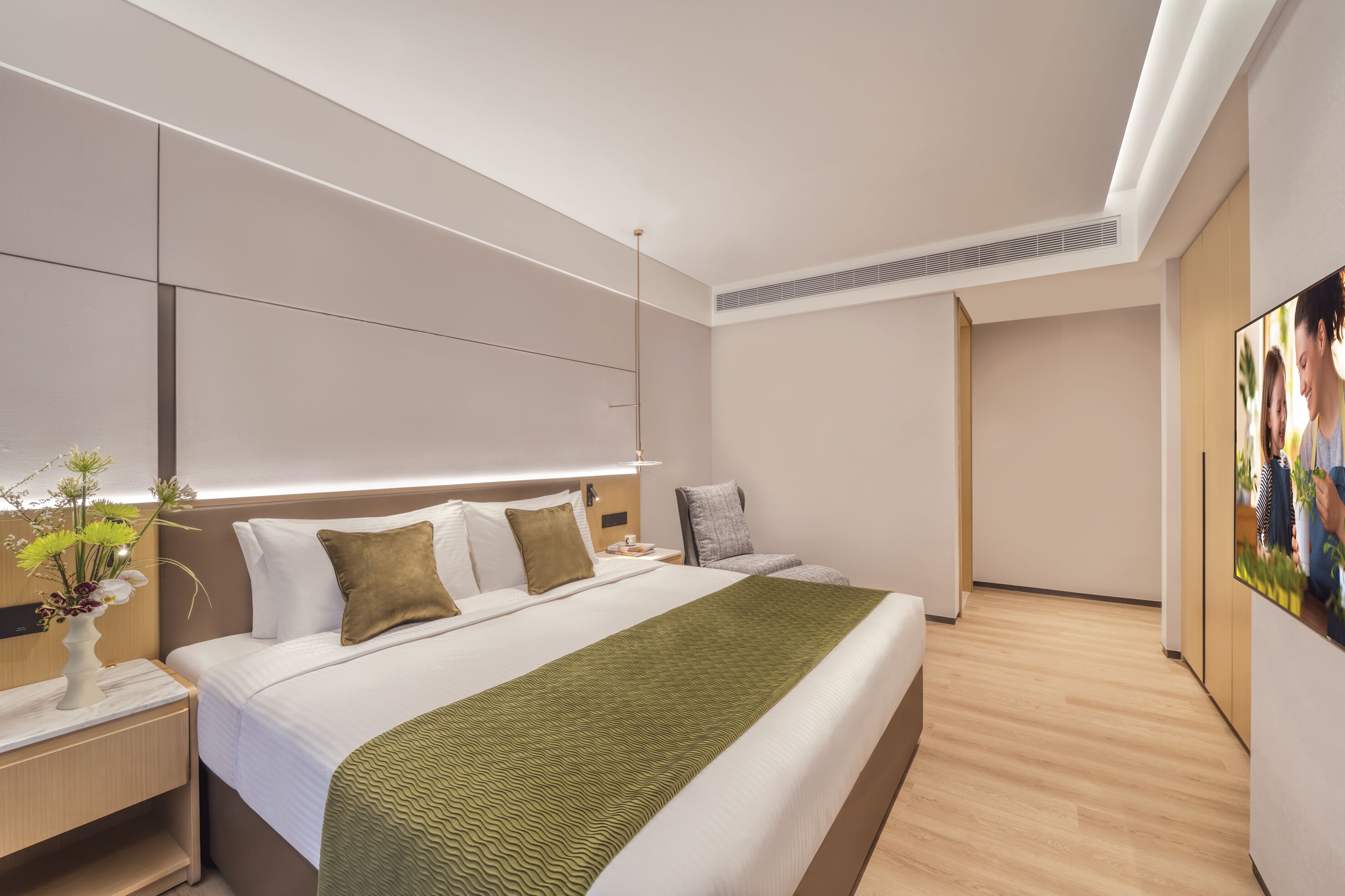 Moderni hotellihuone, jossa on suuri sänky, yöpöydät, yövalaisin, seinälle asennettu televisio ja taulu seinällä.