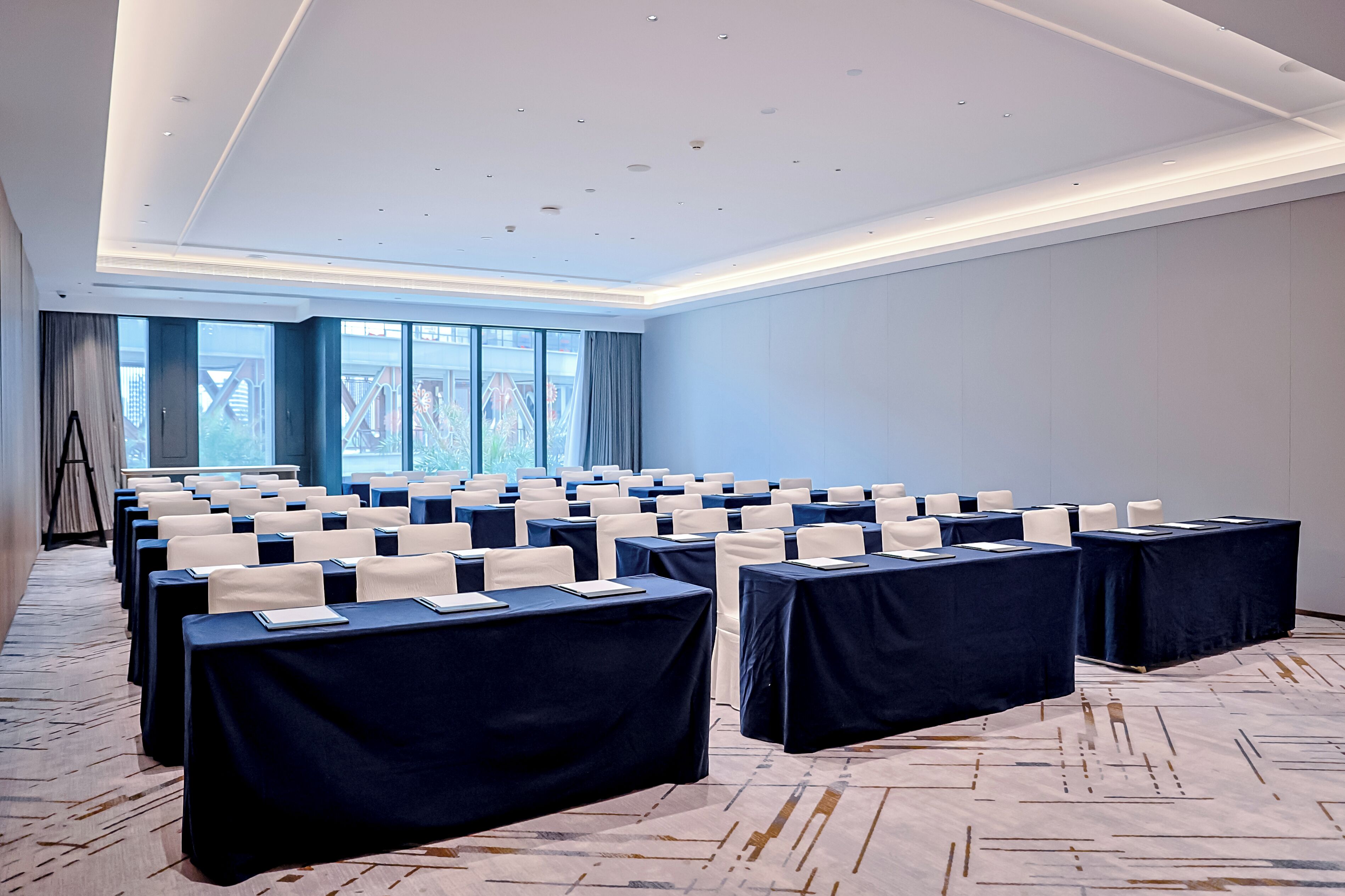 Un salón de conferencias con filas de mesas, sillas y un ventanal grande.