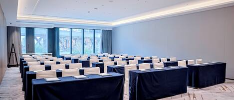 Un salón de conferencias con filas de mesas, sillas y un ventanal grande.