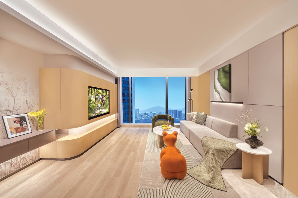 A modern living room with a sofa, a coffee table, a TV, and a large window with a city view.