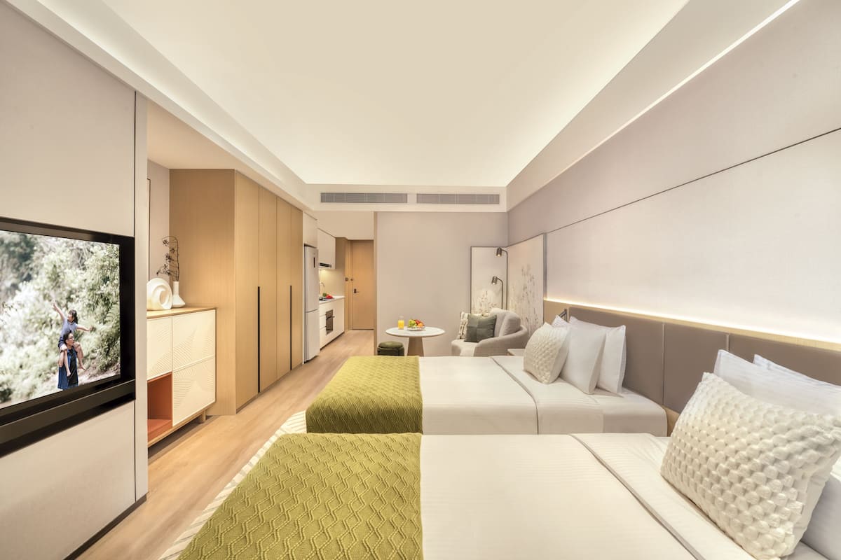 A modern hotel room with a TV, a sofa, a bed, and a small kitchen area.