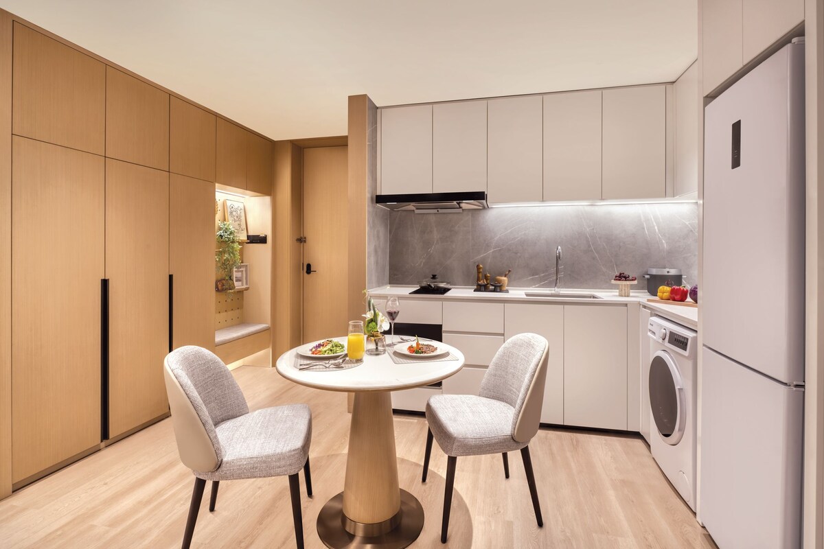 Una cocina moderna con zona de comedor, armarios de madera, lavadora integrada y una mesa redonda con sillas.
