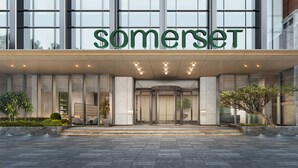 A modern hotel entrance with a large glass facade, a prominent 'Somerset' sign, and a well-lit entrance area.