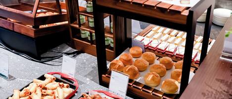 A buffet with various food items including pastries, rolls, and desserts.