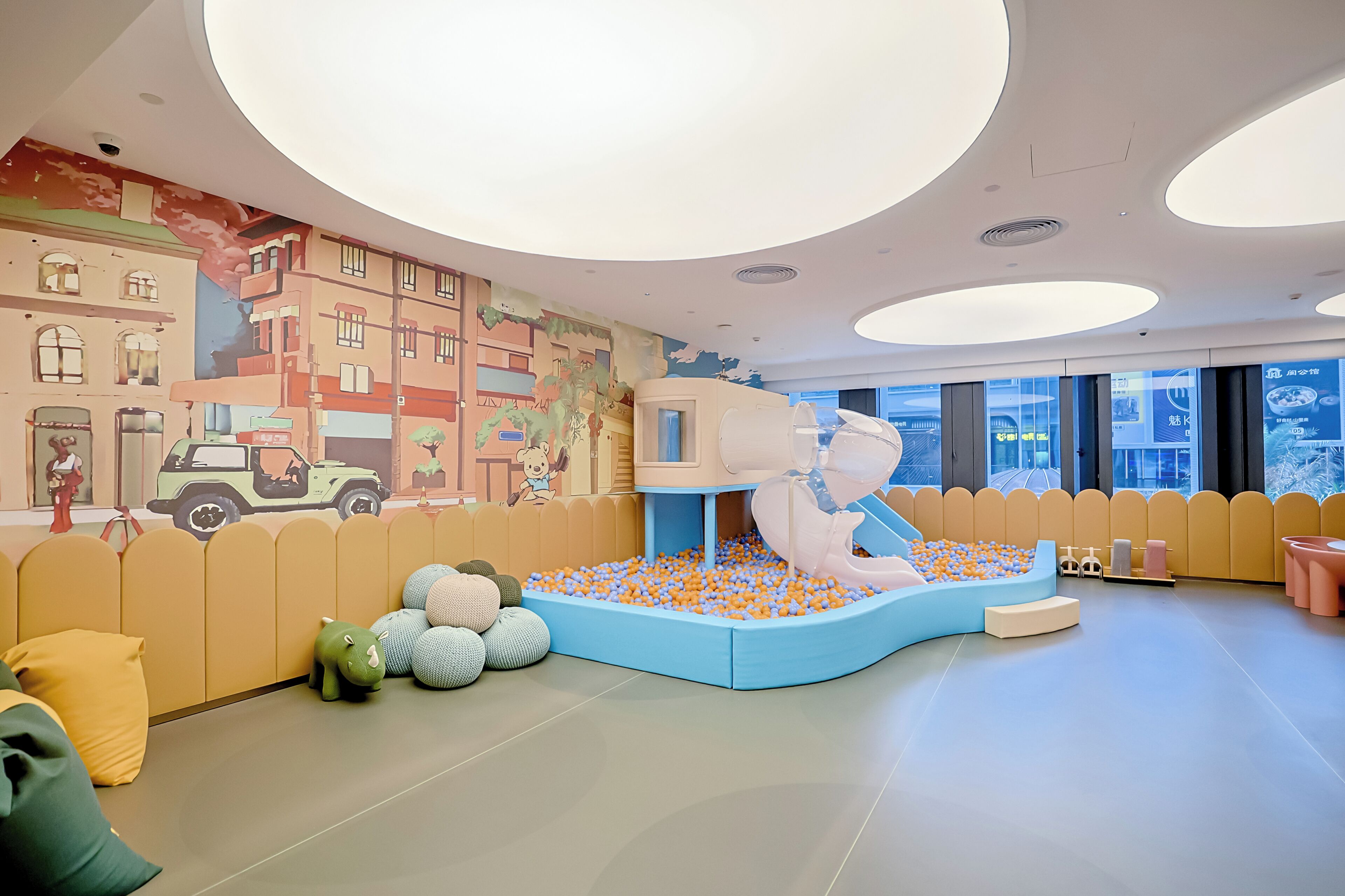 A children's play area with a ball pit, soft play structures, and a mural of a cityscape.