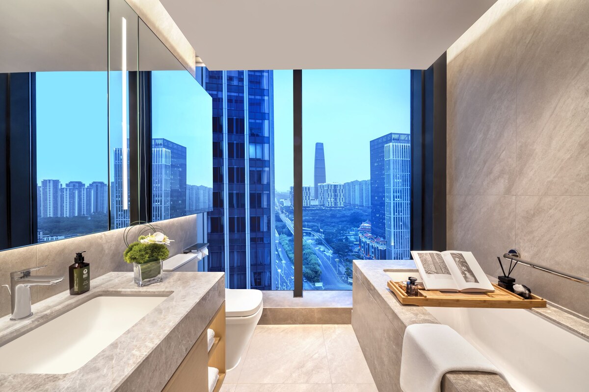 A modern bathroom with a city view, a large mirror, and a wooden vanity.