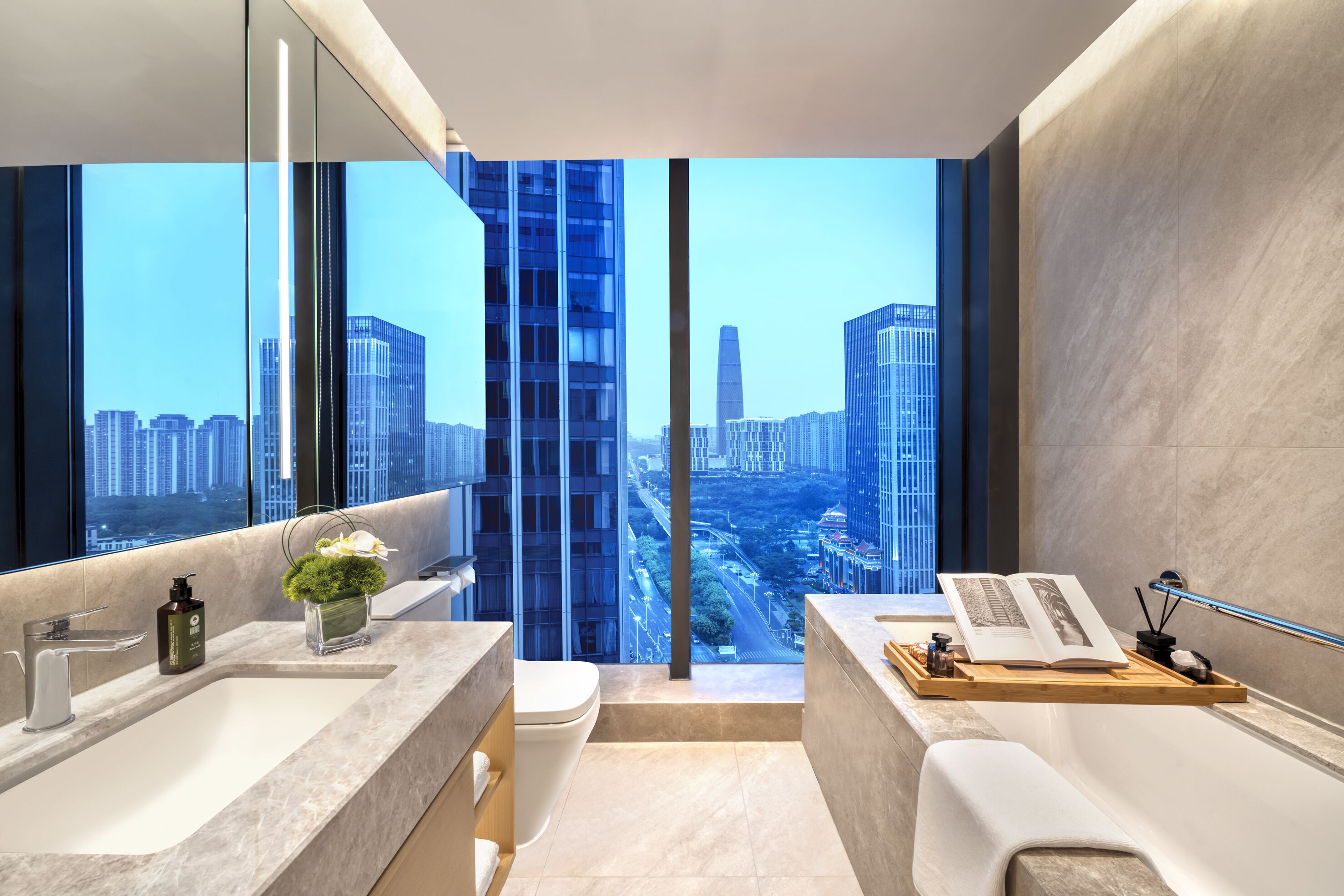 A modern bathroom with a large window, a bathtub, a vanity with a mirror, and a toilet.