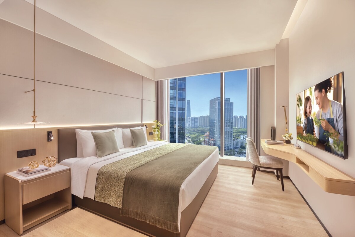 Una habitación de hotel moderna con una cama grande, un escritorio, una silla y vista a la ciudad.