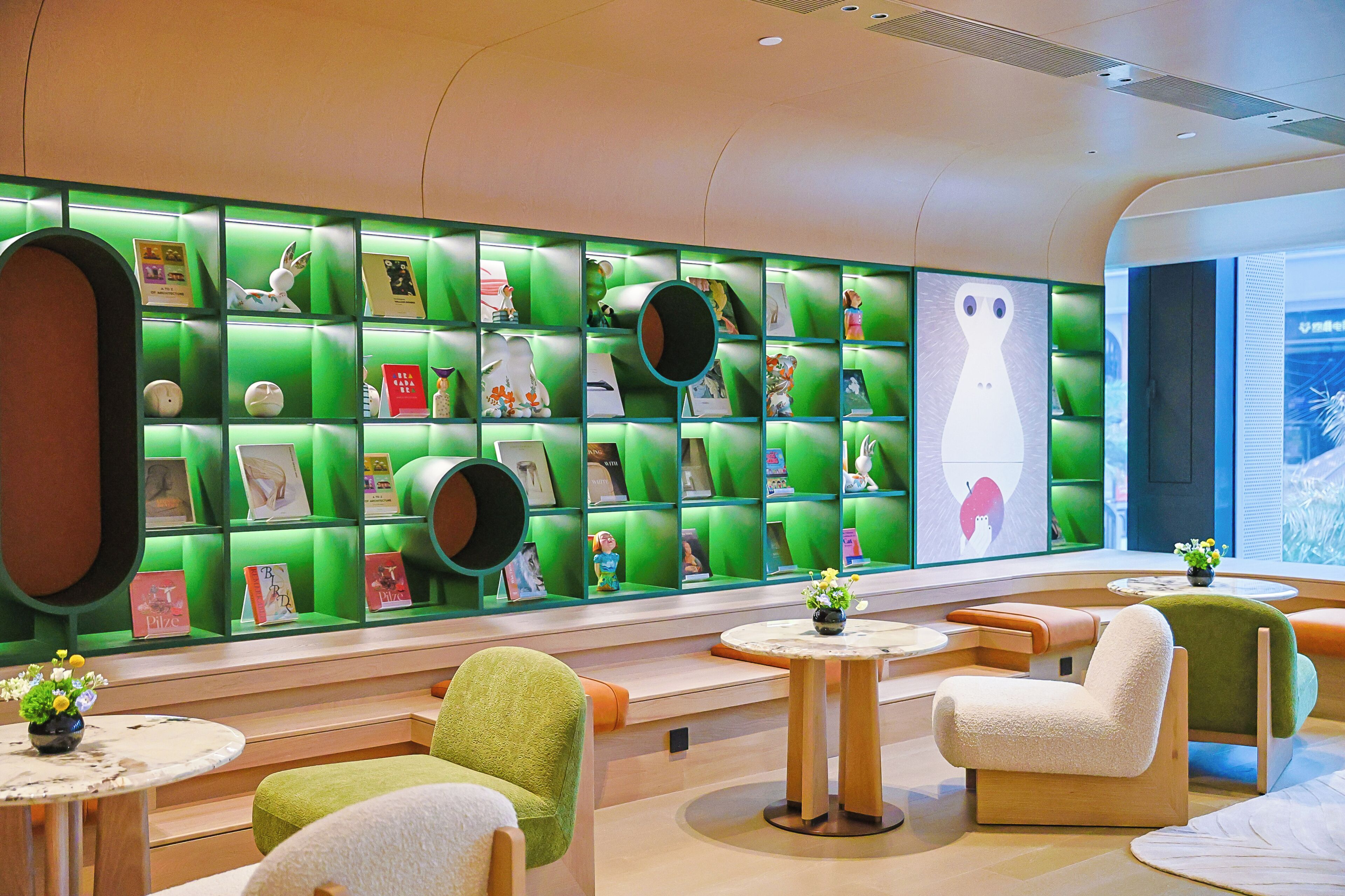 Un interior moderno con estanterías verdes, asientos mullidos y una gran composición mural.