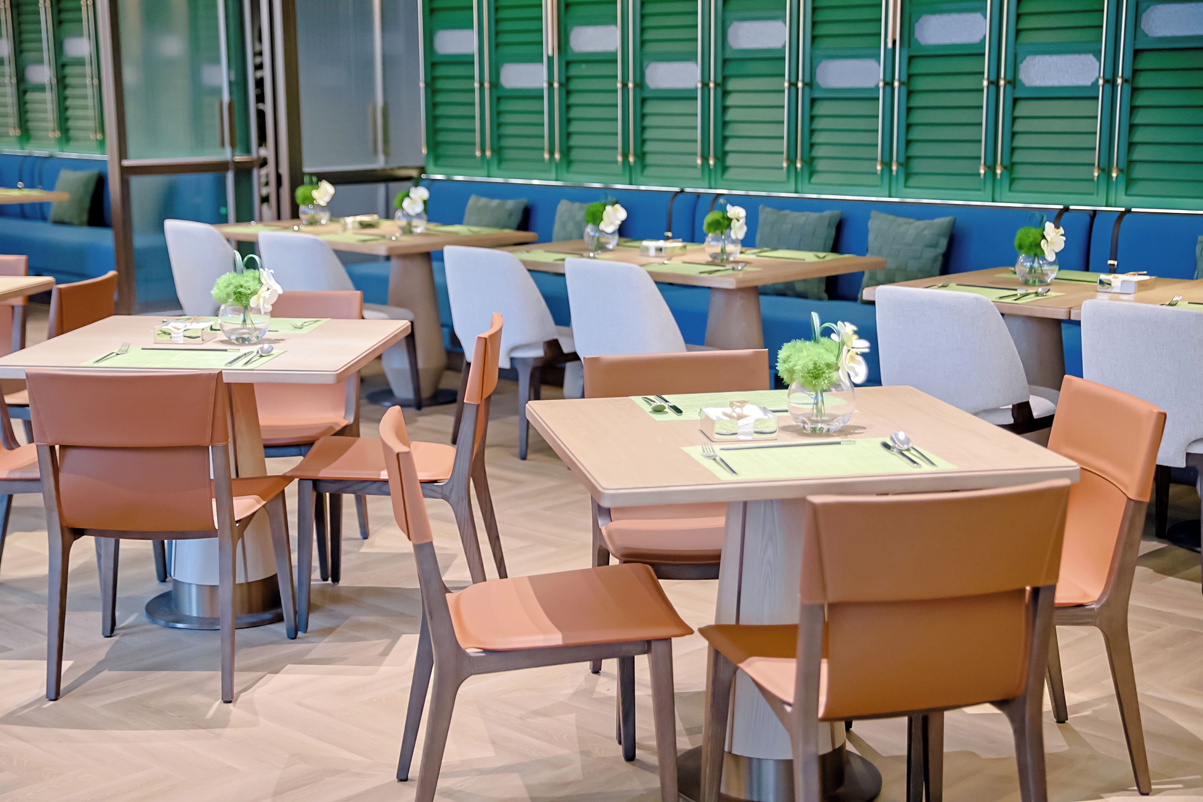 A restaurant with multiple tables and chairs, green window shutters, and a modern interior design.