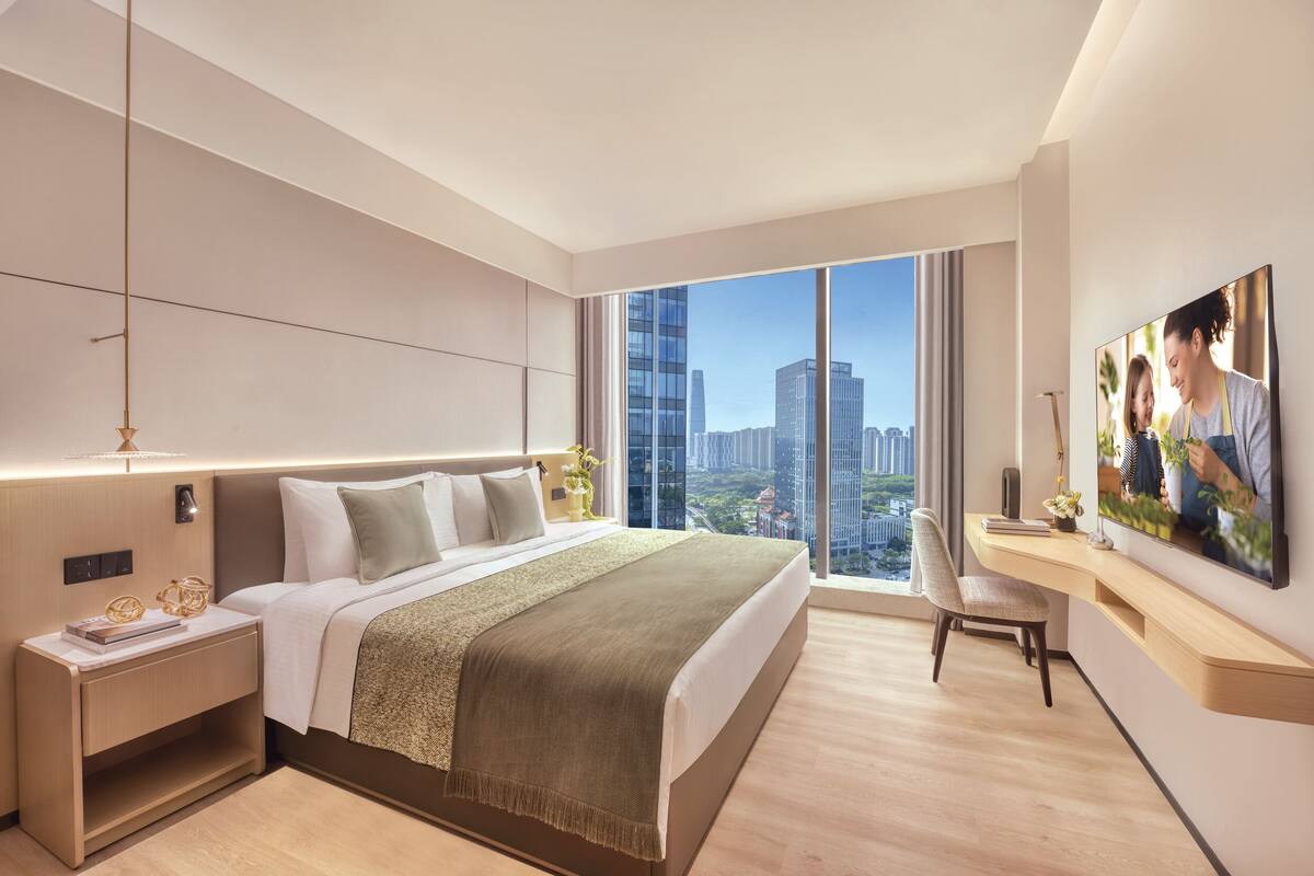 A modern hotel room with a large bed, a desk, a chair, and a city view.