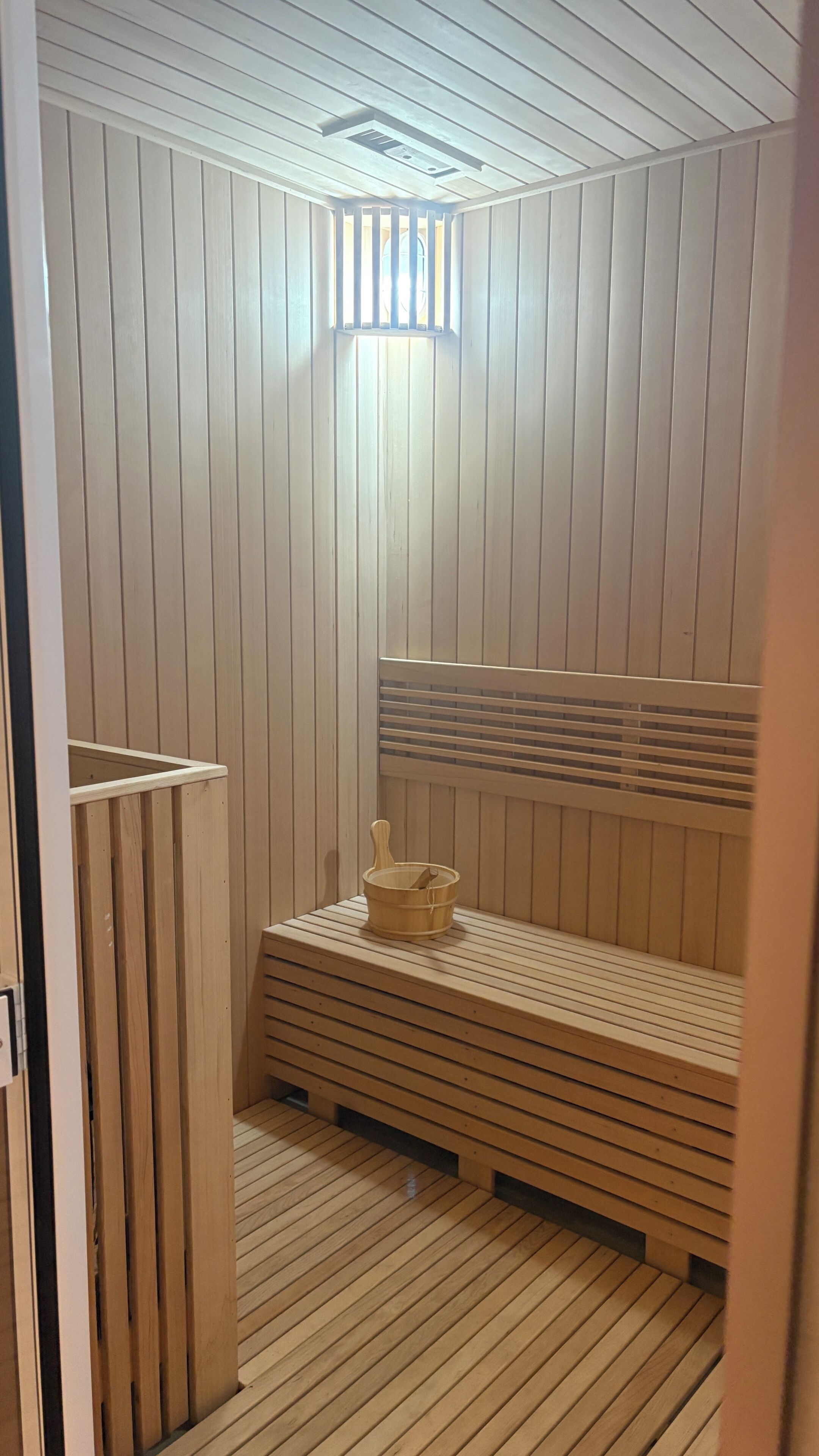 Sala de sauna com ripas de madeira, um banco e um balde de madeira.