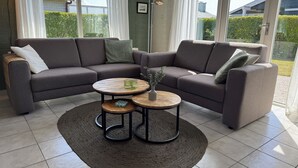En moderne stue med en hjørnesofa, to runde sofaborde og udsigt til det fri gennem store vinduer.