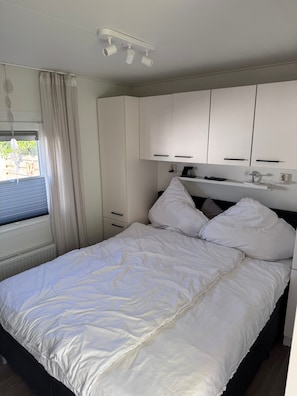 A bedroom with a bed, white curtains, a window, and a ceiling-mounted light fixture. - Chalet 229 (4 persons) (Petten)