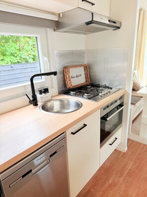 A compact kitchen with a built-in dishwasher, a gas stove, and a window with a view of greenery. - Chalet 229 (4 persons) (Petten)