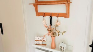 Eine weiße Tür mit einem Holzregal darüber, auf dem sich ein Spiegel, ein Schild, eine Blumenvase und ein kleines schmuckes Haus befinden.