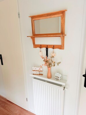 A white door with a wooden shelf above it, holding a mirror, a sign, a vase with flowers, and a small house-shaped ornament. - Chalet 229 (4 persons) (Petten)