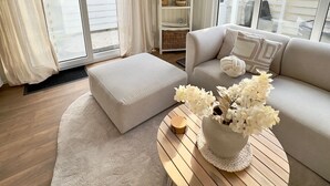 Ein Wohnzimmer mit einer Couch, einem Hocker und einem runden Couchtisch mit Blumen.