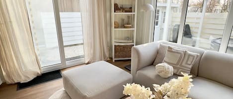 Una sala de estar con sofá, reposapiés y una mesa redonda de centro con flores.