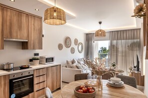 A modern kitchen with wooden cabinets, a built-in oven, and a dining area with a round table and chairs. - 2 Bedroom Apartment In Fig Tree Bay (protaras)