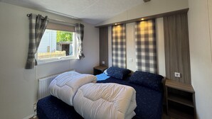 Quarto com cama, janela com cortinas, radiador e prateleira embutida na parede.