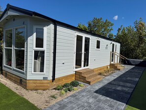 A single-story mobile home with a large sliding glass door, a small window, and a wooden deck. - J 041 New chalet! (more photos to follow) (Petten)